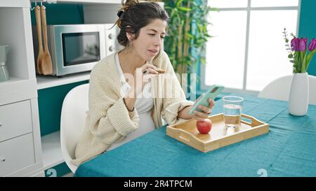 Junge schwangere Frau beim Frühstück, die sich im Speisesaal ein Video auf einem Smartphone ansieht Stockfoto