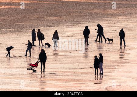 Abendlicht, das Menschen am Fistral Beach bei Ebbe in Newquay in Cornwall in Großbritannien umhüllt. Stockfoto