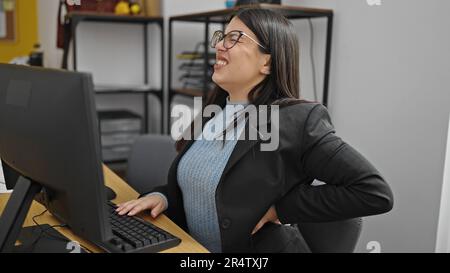 Junge hispanische Geschäftsfrau, die im Büro unter Rückenschmerzen leidet Stockfoto