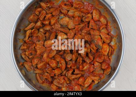 Hühnerherzen mit Petersilie und Tomaten werden in einer Metallpfanne gebraten. Hausmannskost oder kulinarisch. Hausgemachtes Gericht. Stockfoto