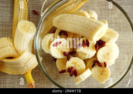 Reife frische Bananenscheiben und trockener Obstsalat mit Goji-Beeren in einer Glasschüssel Stockfoto