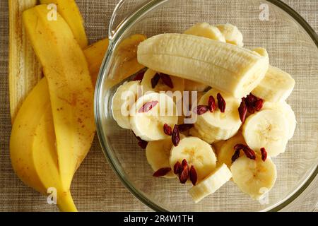 Reife frische Bananenscheiben und trockener Obstsalat mit Goji-Beeren in einer Glasschüssel Stockfoto