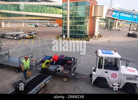 Flughafenmitarbeiter laden Gepäck aus einem Flugzeug in ein Gepäckfahrzeug. Flughafen Tiflis, Georgia. Flughafen Frachtwaggons, Gepäcktraktoranhänger Stockfoto