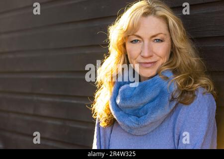 Attraktive, durchdachte, lächelnde, glückliche Frau mittleren Alters draußen im goldenen Sonnenlicht Stockfoto