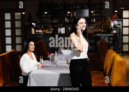 Die junge Frau langweilt sich, während ihre Freundin geschäftlich telefoniert. Stockfoto