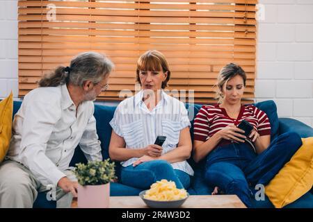 Familienmitglieder aus mehreren Generationen genießen eine schöne Zeit zusammen, indem sie Fernsehen, Snacks und Gespräche teilen und neue entdecken Stockfoto