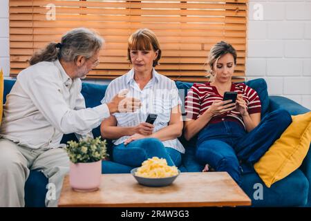 Familienmitglieder aus mehreren Generationen genießen eine schöne Zeit zusammen, indem sie Fernsehen, Snacks und Gespräche teilen und neue entdecken Stockfoto