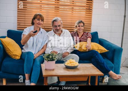 Familienmitglieder aus mehreren Generationen genießen eine schöne Zeit zusammen, indem sie Fernsehen, Snacks und Gespräche teilen und neue entdecken Stockfoto