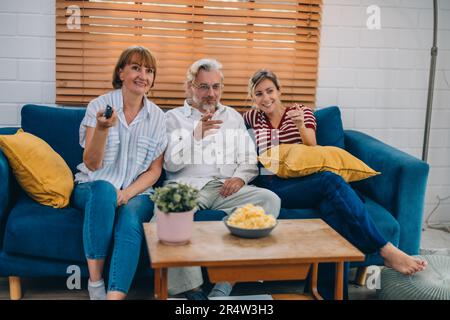 Familienmitglieder aus mehreren Generationen genießen eine schöne Zeit zusammen, indem sie Fernsehen, Snacks und Gespräche teilen und neue entdecken Stockfoto