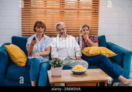 Familienmitglieder aus mehreren Generationen genießen eine schöne Zeit zusammen, indem sie Fernsehen, Snacks und Gespräche teilen und neue entdecken Stockfoto