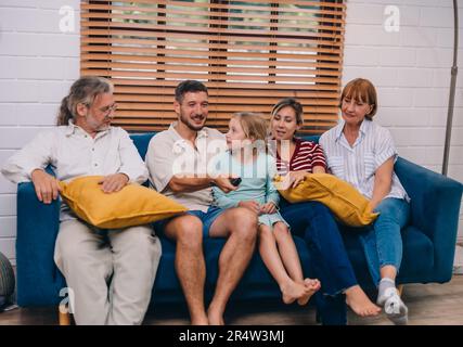 Familienmitglieder aus mehreren Generationen genießen eine schöne Zeit zusammen, indem sie Fernsehen, Snacks und Gespräche teilen und neue entdecken Stockfoto