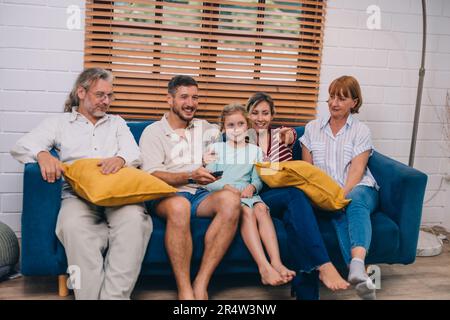 Familienmitglieder aus mehreren Generationen genießen eine schöne Zeit zusammen, indem sie Fernsehen, Snacks und Gespräche teilen und neue entdecken Stockfoto