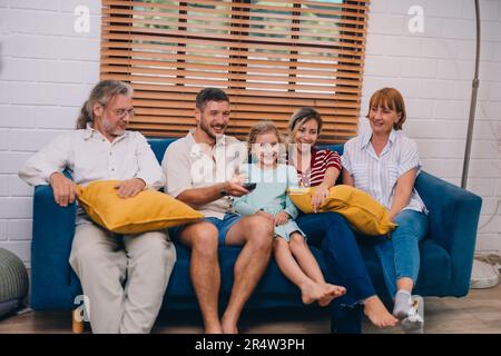 Familienmitglieder aus mehreren Generationen genießen eine schöne Zeit zusammen, indem sie Fernsehen, Snacks und Gespräche teilen und neue entdecken Stockfoto