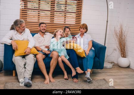 Familienmitglieder aus mehreren Generationen genießen eine schöne Zeit zusammen, indem sie Fernsehen, Snacks und Gespräche teilen und neue entdecken Stockfoto