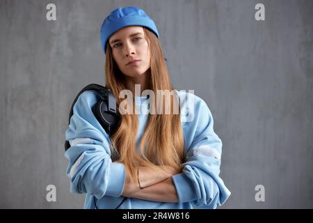 Ein junges, hübsches, langhaariges Mädchen in einem blauen Pullover und einem lustigen Hut mit schwarzen DJ-Kopfhörern auf der Schulter hat ihre Hände gefaltet. Musik, Spaß und Entspannung Stockfoto