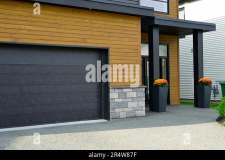 Blick auf die Straße eines modernen Vorstadthauses. Die Außenwände sind graue Ziegel, orangefarbenes Beistellholz und ein Metall aus Wohnimmobilien. Stockfoto