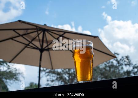 Ein klares Pint Trinkglas gefüllt mit kaltem Schaum von einem Lagerale. Das irische rote Ale-Pint befindet sich an der Kante eines Metall-Terrassentisches in einer Mikrobrauerei. Stockfoto