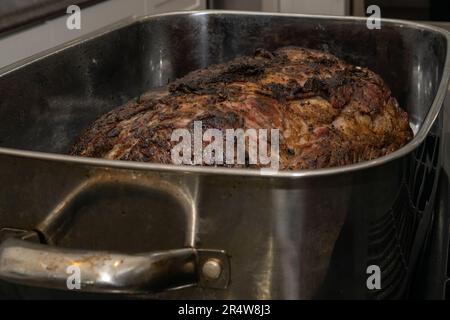 Ein großer, gut gemachter Angus-Rinderbraten, gekocht in einer Bratpfanne mit Zwiebeln und Knoblauch. Die glänzende Metallwanne ist rechteckig und hat Griffe. Stockfoto