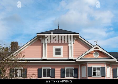 Ein mehrstöckiges, rosafarbenes Haus im viktorianischen Stil mit weißen Zierleisten. Das Gebäude hat mehrere kleine, viergläserne Fenster mit schwarzen Fensterläden. Stockfoto