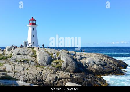 Malerische Peggy's Cove mit einem hohen weißen Leuchtturm und einem roten Turm auf der Spitze. Die Betonstruktur hat drei Fenster. Da sind Leute, die unter uns laufen. Stockfoto