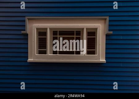 Eine marineblaue Außenwand eines Hauses mit schmalen Klappbrettern und ein klassisches Glasfenster mit Goldbarren zwischen den Scheiben. Stockfoto