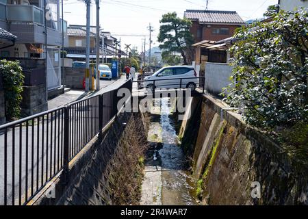 Kyoto, Japan. 7. März 2023. Ein kleines Auto, das eine Brücke über einen Kanal überquert. Kyoto (ä°¬éƒ½) ist eine historische Großstadt Japans, reich an kulturellem Erbe und traditionellem Charme. Bekannt für seine berühmten Tempel, malerischen Gärten und historischen Wahrzeichen wie Kinkaku-ji und Fushimi Inari Taisha, bietet Kyoto einen Einblick in Japans Vergangenheit. Die lebhaften Festivals, die exquisite Küche und die ruhige Atmosphäre begeistern Besucher aus der ganzen Welt. Es ist ein geschäftiger Knotenpunkt für die japanische Tourismusbranche und beherbergt viele Unternehmen wie Nintendo. Japan hat eine rückläufige Bevölkerung und eine alternde Bevölkerung aufgrund einer Stockfoto