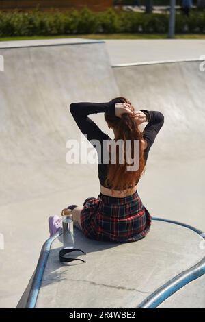 Eine Skaterin sitzt auf einer Rampe mit einer Glasflasche Wasser. Coole junge Roller, die an einem sonnigen Sommertag in einem Skatepark chillen Stockfoto