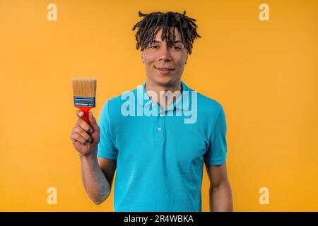 Junger afrikanischer Künstler mit Pinsel auf gelbem Hintergrund. Kreative Person. Stockfoto