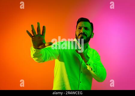 Ein bärtiger, gutaussehender Mann in weißem Hemd, der sich in Neonlicht vor dem Hintergrund des Gradientenstudios postet. Innere Welt Stockfoto