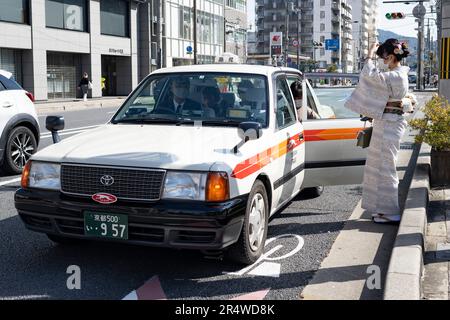 Kyoto, Japan. 7. März 2023. Frauen in traditionellen japanischen Kimonos steigen im Urlaub in ein Taxi. Kyoto (ä°¬éƒ½) ist eine historische Großstadt Japans, reich an kulturellem Erbe und traditionellem Charme. Bekannt für seine berühmten Tempel, malerischen Gärten und historischen Wahrzeichen wie Kinkaku-ji und Fushimi Inari Taisha, bietet Kyoto einen Einblick in Japans Vergangenheit. Die lebhaften Festivals, die exquisite Küche und die ruhige Atmosphäre begeistern Besucher aus der ganzen Welt. Es ist ein geschäftiger Knotenpunkt für die japanische Tourismusbranche und beherbergt viele Unternehmen wie Nintendo. Japan hat eine rückläufige Bevölkerung und Stockfoto