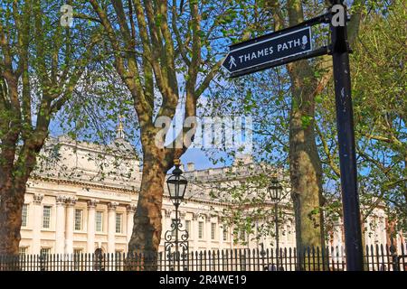 Wegweiser zum Themsenpfad entlang des Flusses in Greenwich, London, mit historischen Gebäuden, die durch Bäume im Hintergrund sichtbar sind Stockfoto