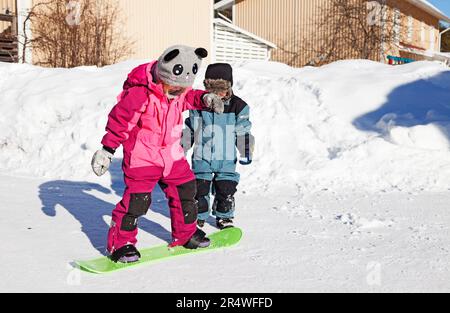 Umea, Norrland Schweden - 11. März 2023: Zwei Geschwister spielen mit Snowboard im Schnee Stockfoto