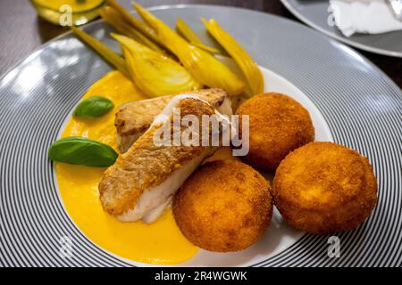 Filet vom Kabeljau, Polenta-Krocket in Karotten- und Orangensaft, marinierter Fenchel auf gestreiftem Teller. Glutenfreies Essen, gutes Essen, Nahaufnahme. Stockfoto