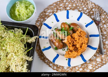 Teller mit gebratener älterer Blume in Teig und Kartoffel, älterer Blüten auf Backform und Gurkensalat auf dem Tisch. Stockfoto