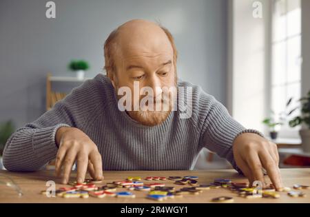 Senior-Mann mit Alzheimer-Krankheit sitzt am Schreibtisch, macht Rätsel und spielt mit Alphabet Stockfoto