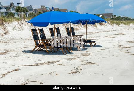 Sonniger Tag am Strand auf Hilton Head Island, South Carolina. Reservierte Liegen und blaue Sonnenschirme warten auf Besucher. Stockfoto