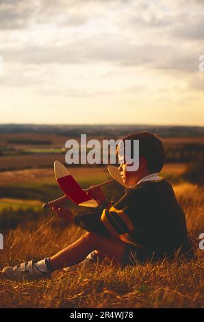 England. Kinder. Der Junge sitzt am Hang mit seinem Modellflugzeug. Stockfoto