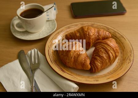 Nahaufnahme eines Tisches, auf dem es ein Frühstück mit Kaffee und Butter Croissants neben einem Mobile gibt Stockfoto