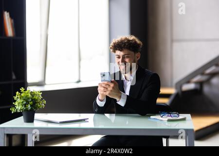 Lächelnder Geschäftsmann mit Smartphone im Büro. Digitale Technologieanwendungen und -Lösungen für die Geschäftsentwicklung Stockfoto