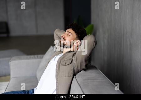 Hübscher junger Mann hält die Hände hinter den Kopf beim Schlafen auf der Couch Stockfoto