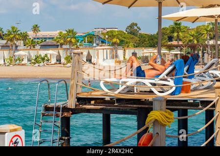 Antalya; Türkei-September 11; 2022: Leute sonnen sich im Sommer auf Liegen unter Sonnenschirmen auf einem hölzernen Pier. Antalya eine beliebte Stadt für Russisch, Ukrainien Stockfoto