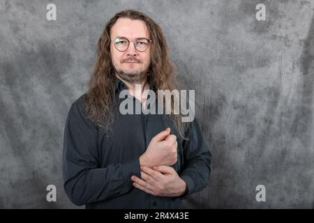 Ein Mann in einem schwarzen Hemd, lange Haare und Brille Stockfoto