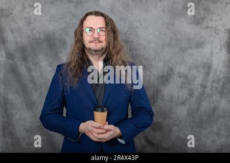 Ein Mann allein in einer blauen Jacke, langen Haaren, Brille, ein Glas in den Händen Stockfoto