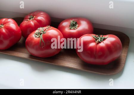 Köstliche rote reife Sommertomaten aus Rindfleisch auf einem Holztablett Stockfoto