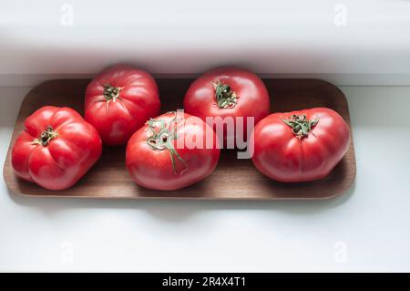 Köstliche rote reife Sommertomaten aus Rindfleisch auf einem Holztablett Stockfoto