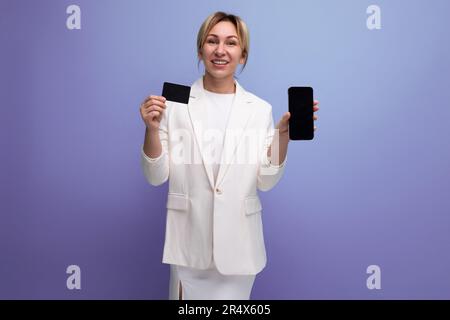 Junge blonde geschäftsfrau aus europa in weißer Jacke und Kleid mit einer Karte und einem Telefonmodell Stockfoto