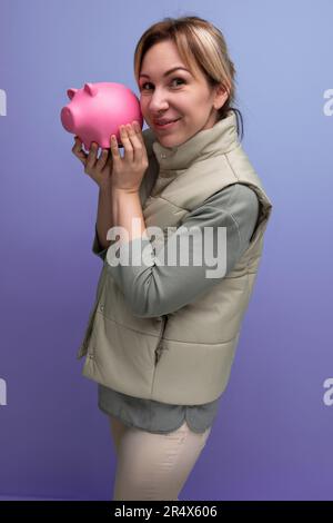 Die junge blonde Frau wird das gesammelte Geld von der Sparschweinbank in einen Kauf investieren Stockfoto
