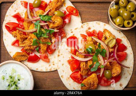 Kochen traditioneller griechischer Gerichte Gyros: Nahaufnahme von Pita-Brot mit Gemüse, Fleisch, Kräutern, Oliven auf rustikalem Holzbrett mit Tzatziki-Sauce Stockfoto