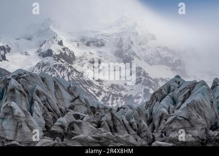 Malerischer Blick auf Gletschereisformationen und schneebedeckte Berge mit nebligen Wolken, die die Gipfel im Hintergrund umgeben; Island Stockfoto