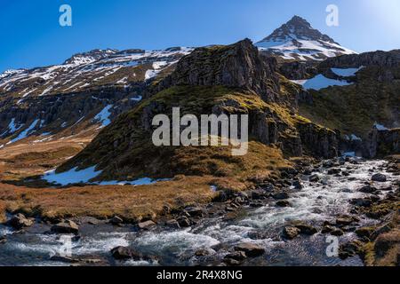 Nahaufnahme eines Flusses, der durch die atemberaubende Berglandschaft eines Fjords mit klarem, blauem Himmel fließt; Ost-Island, Island Stockfoto